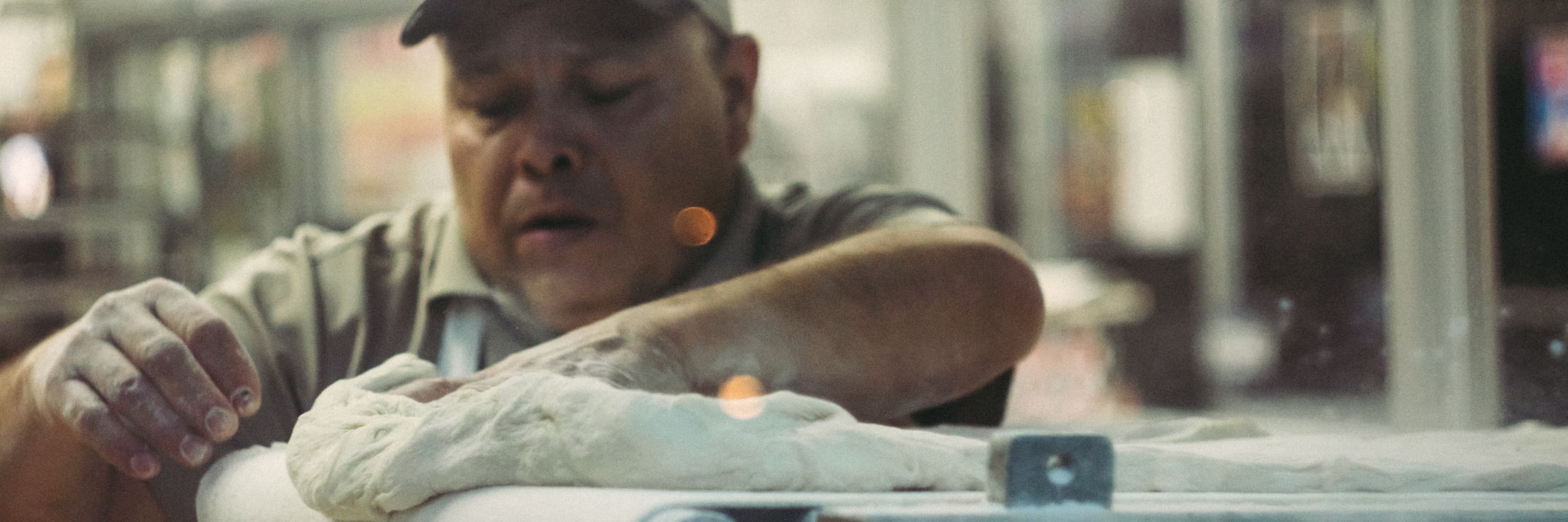A baker working a length of dough through the roller in the bakery's back room.