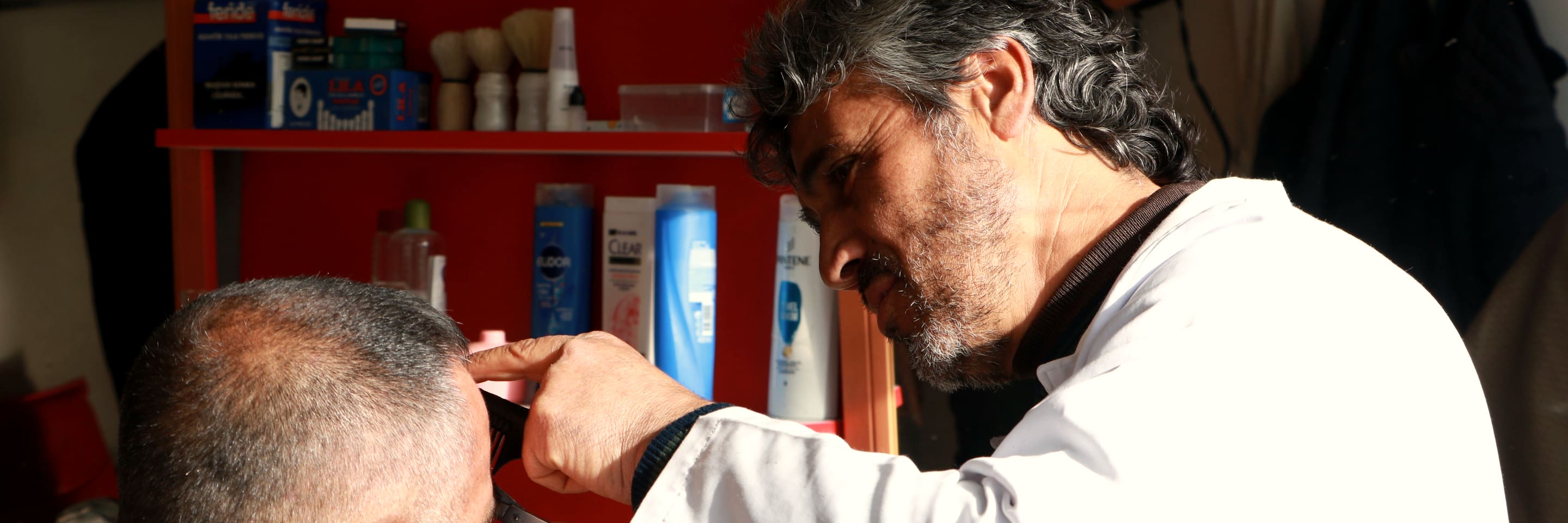 A barber leaning in to finish a client's cut in his shop.