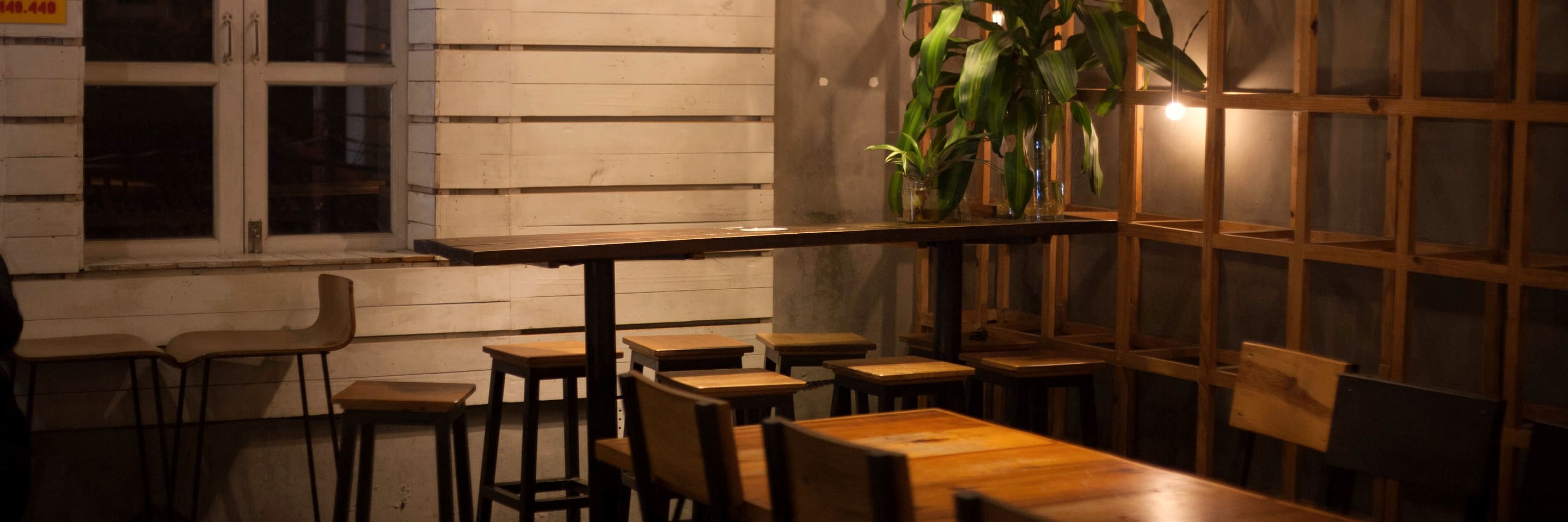 An empty cafe after closing, one wall light still on over the bar stools and the long wooden table.
