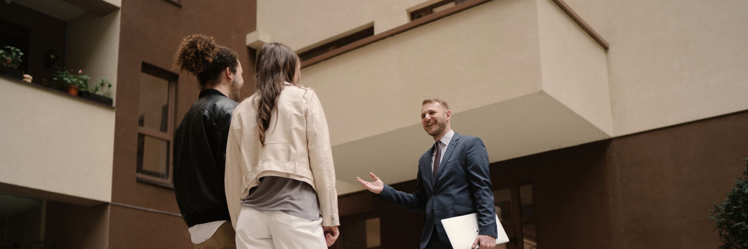 An agent in a suit showing a couple around the courtyard of a residential building.