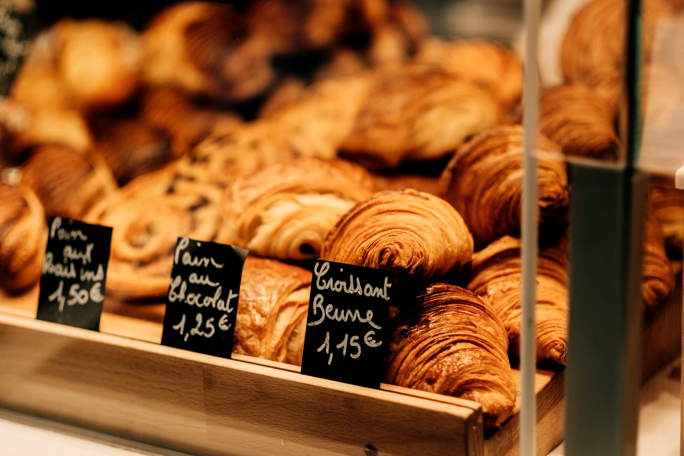 A tray of croissants and pains au chocolat in a bakery window, priced up on chalk cards.