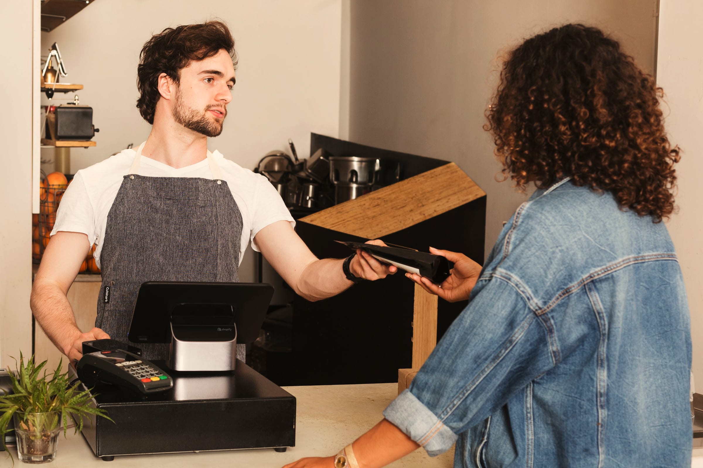 A barista handing the card reader across the counter to a customer paying.