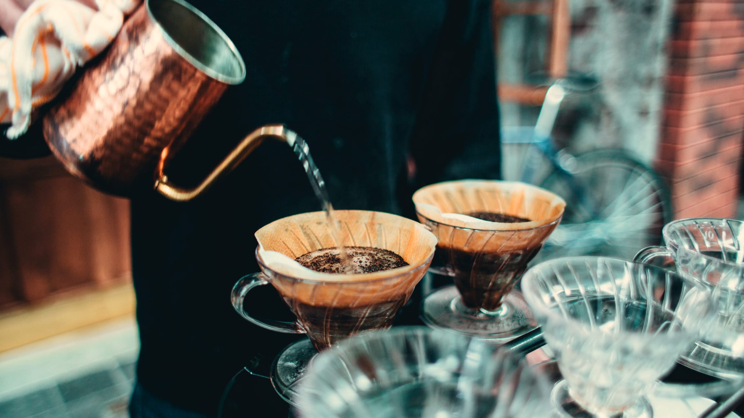 Pour-over coffee being made at a cafe bar, water poured from a copper kettle into paper filters.