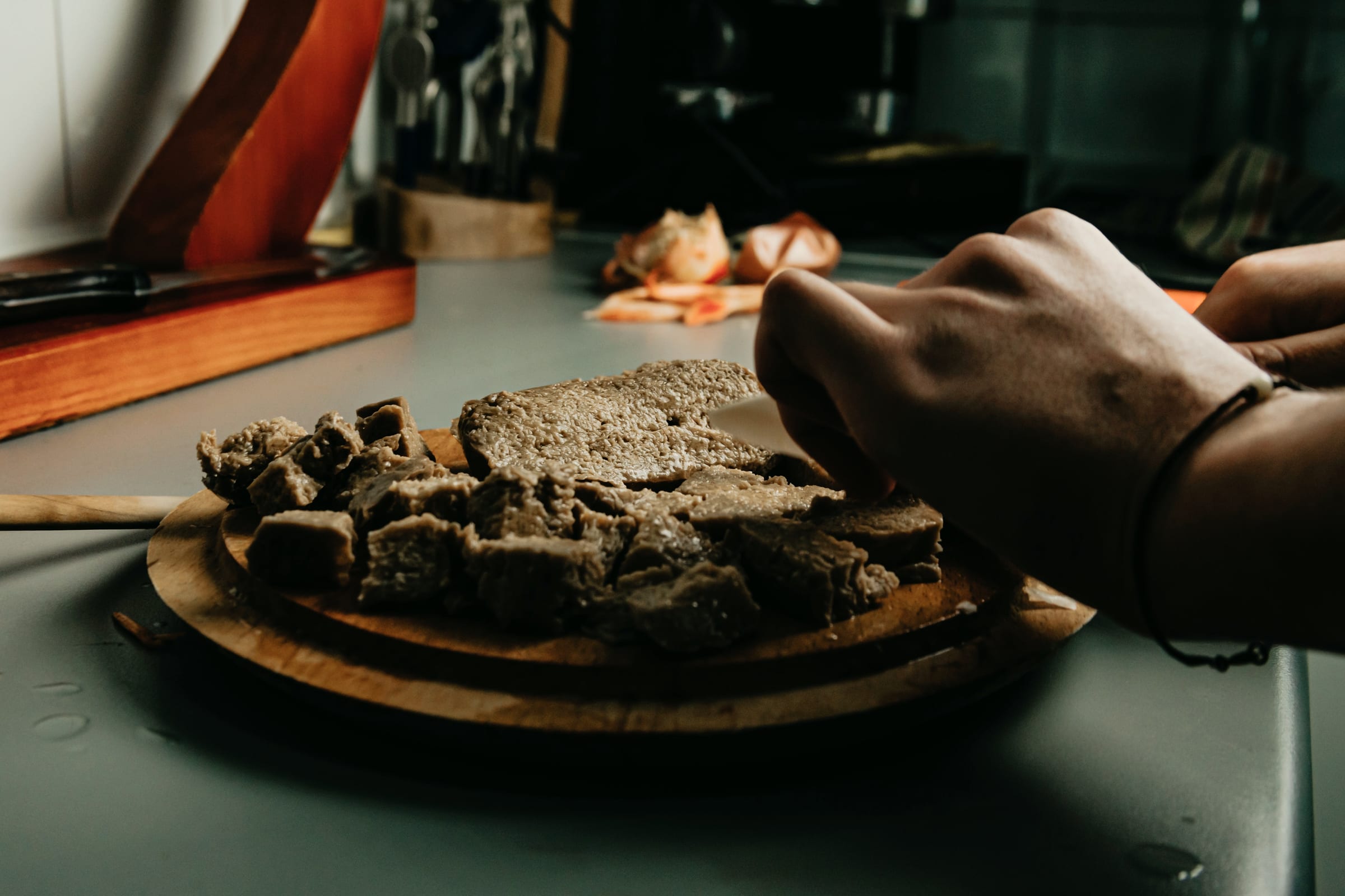 Hands portioning food on a wooden board in a dark kitchen.