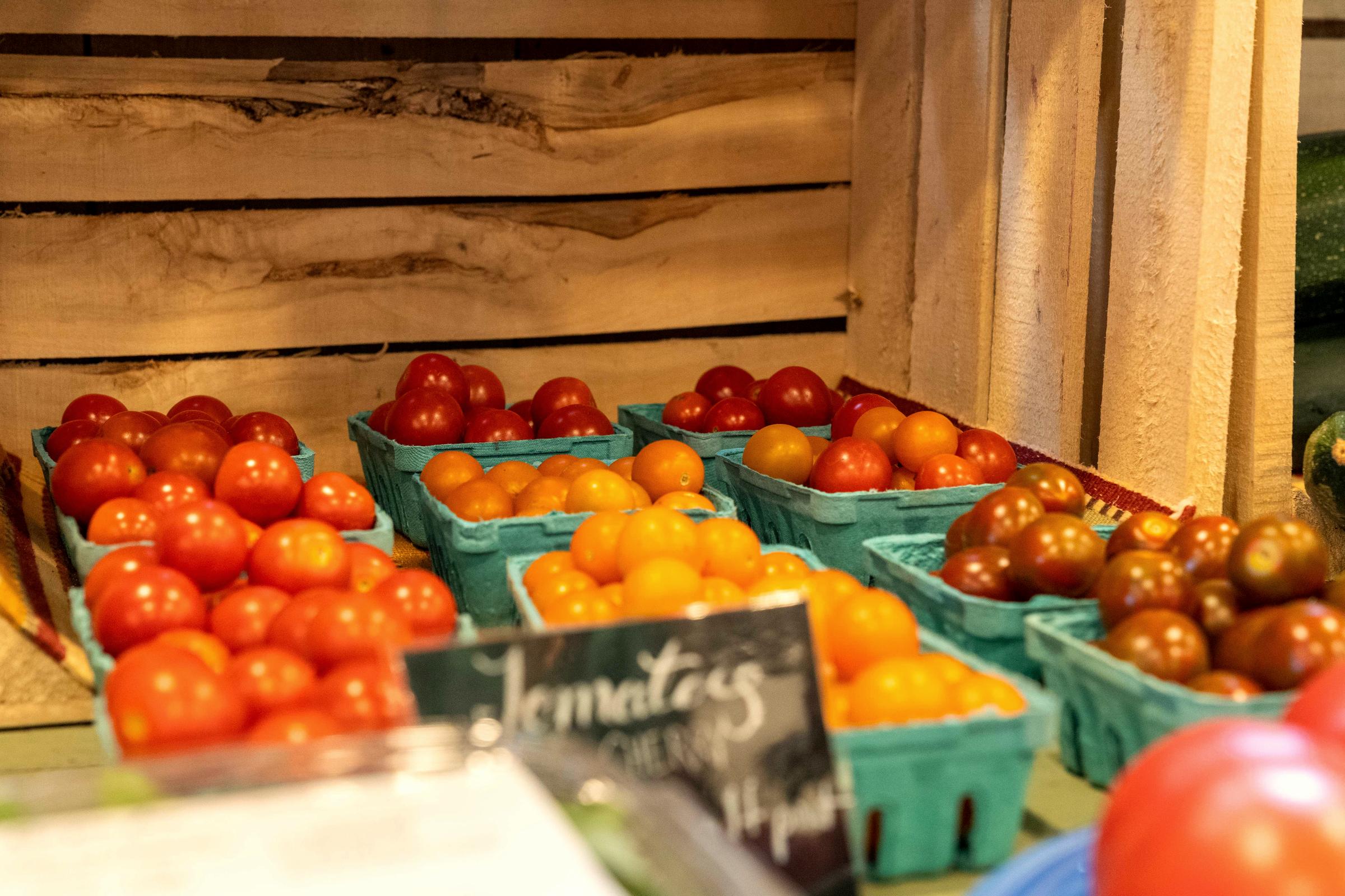 Punnets of red and yellow tomatoes on the rough timber shelf of a roadside farm stand, priced up on a chalk sign.