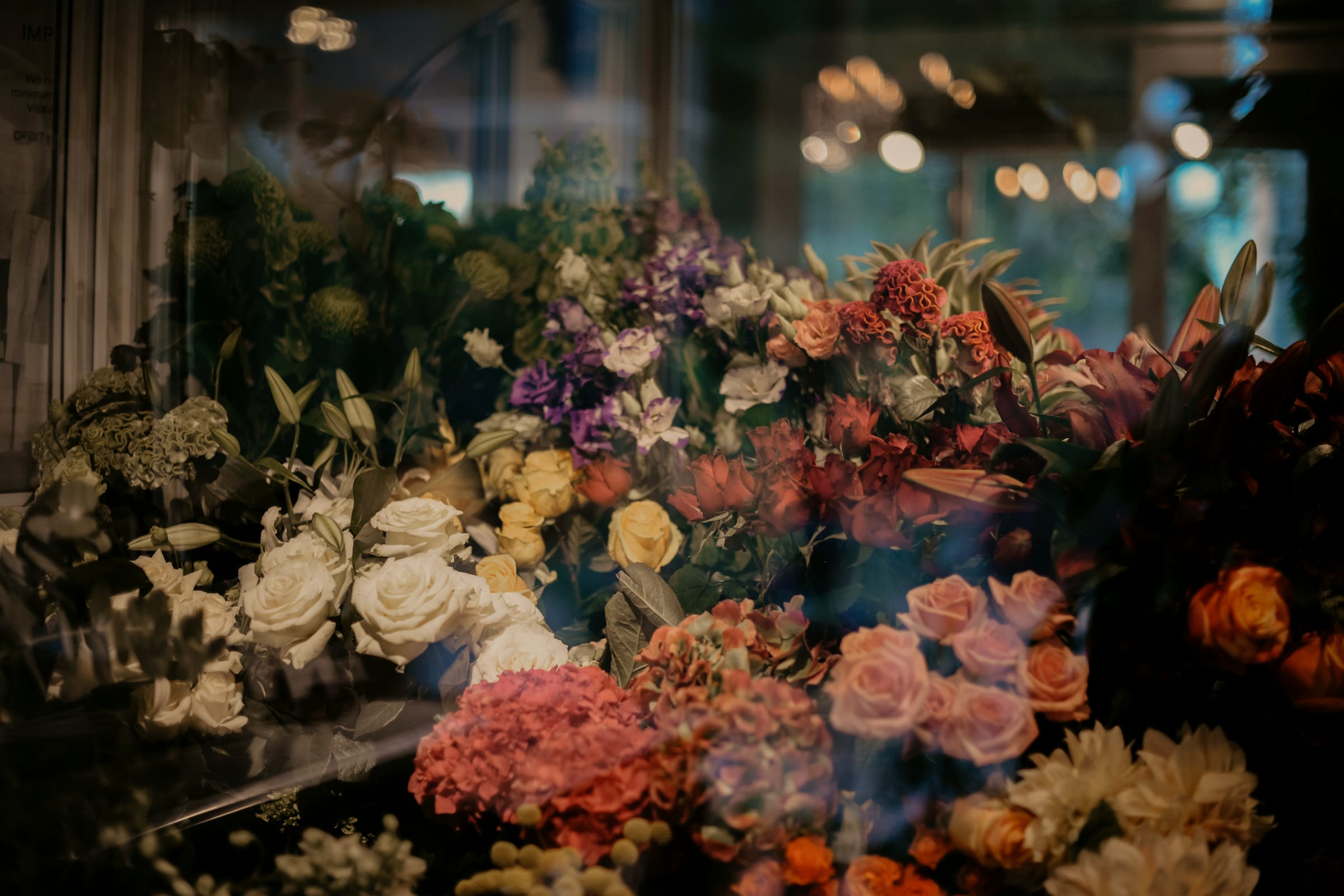 A florist's bouquets massed under warm light, seen through the shop window.