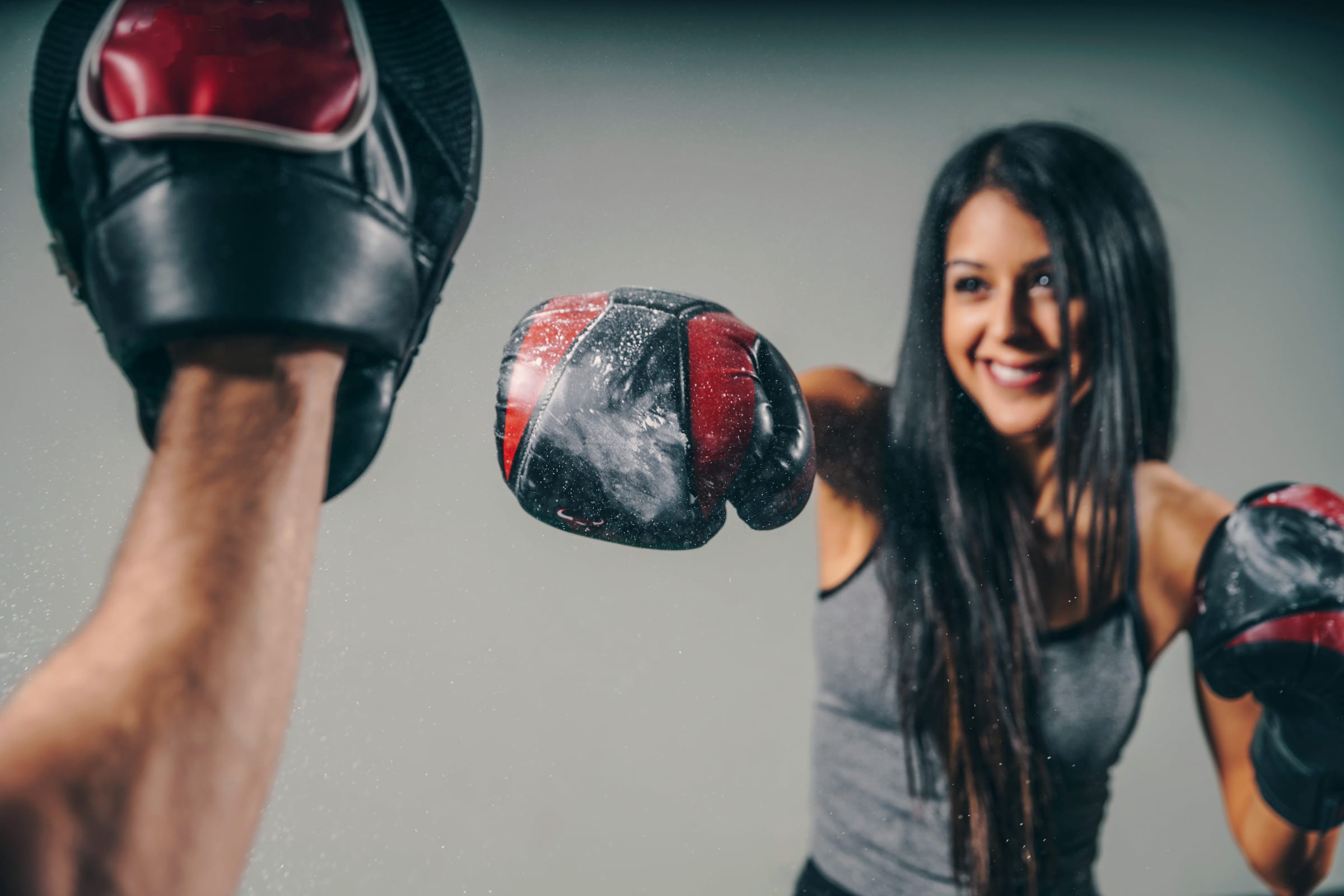 A trainer's focus mitts up while a smiling client in gloves works a combination.