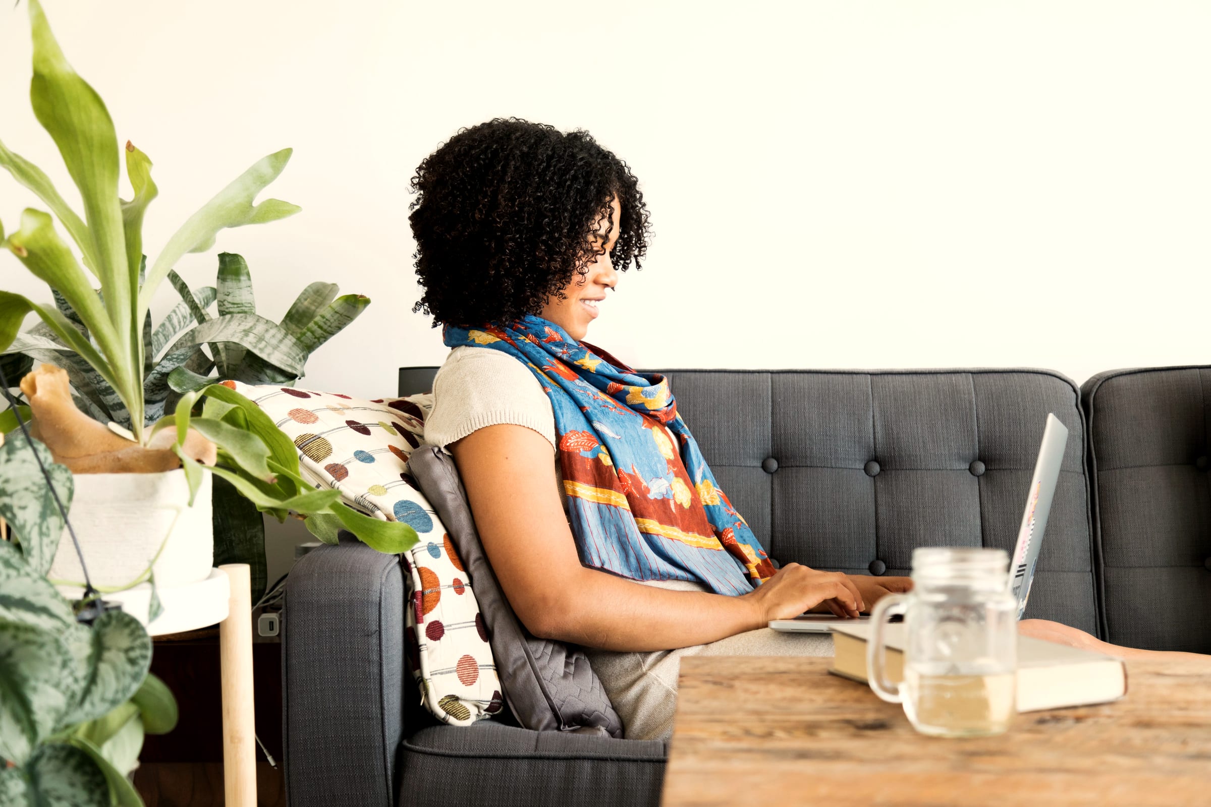 A freelancer working on a laptop at a low table at home, house plants behind her.