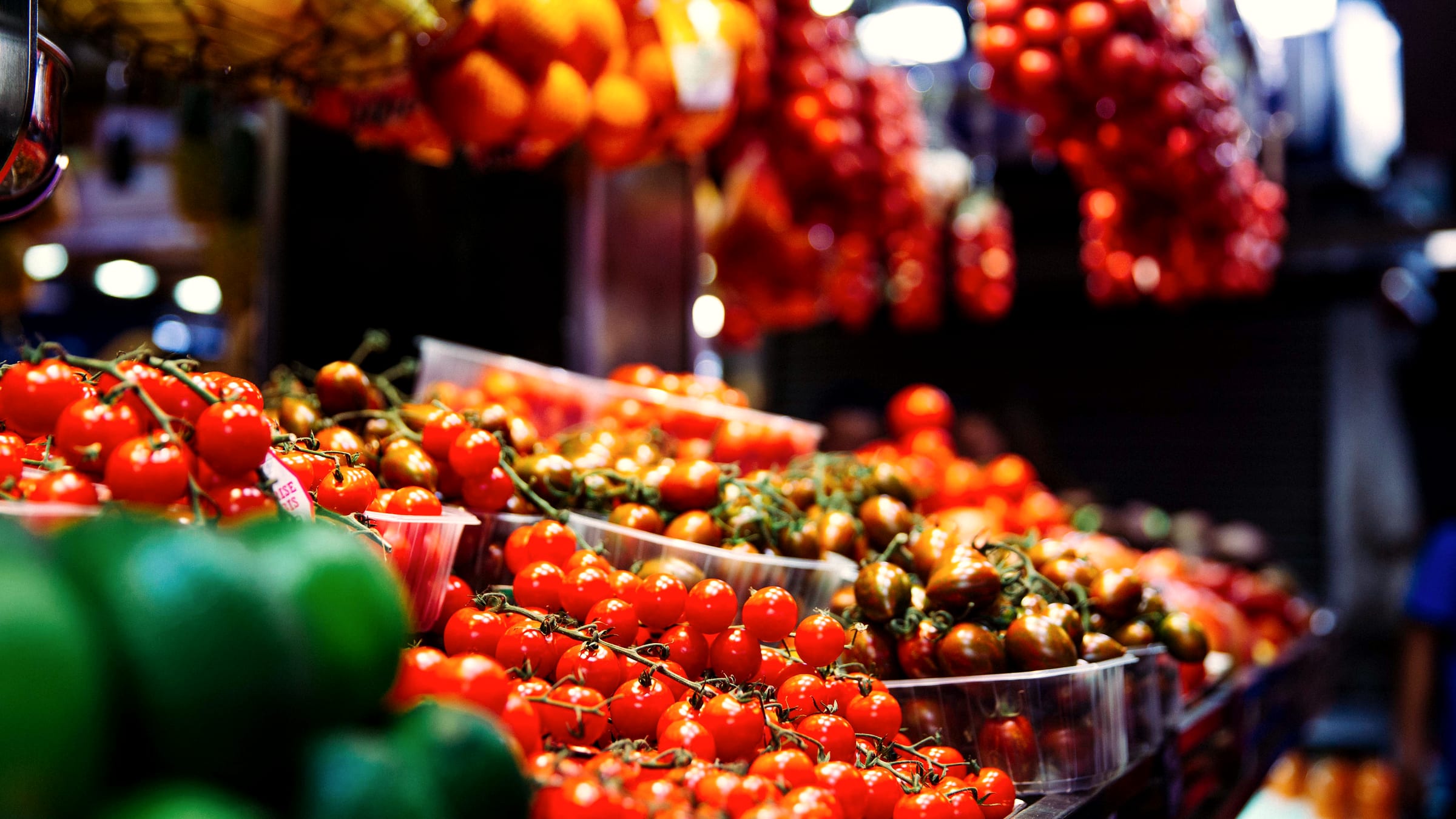 Vine tomatoes piled high on a market stall, hanging bunches strung above.