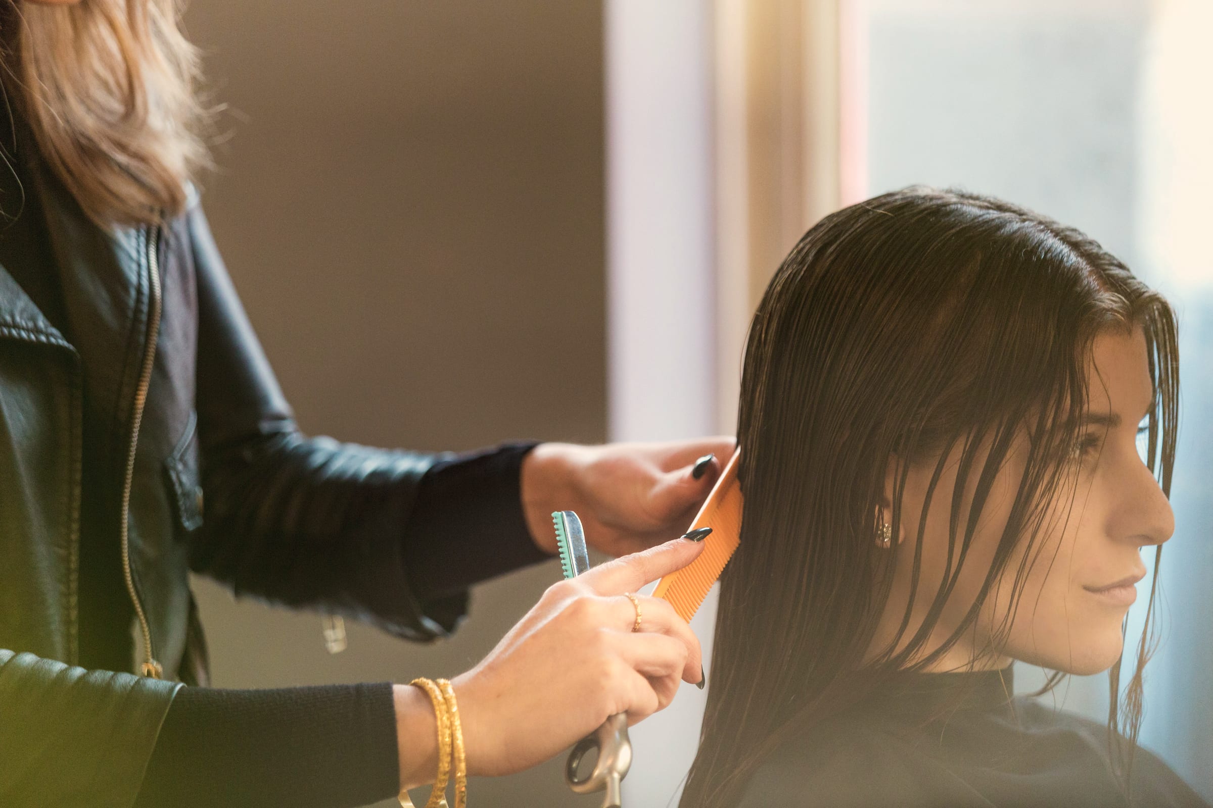 A stylist combing a seated client's hair through in a salon.